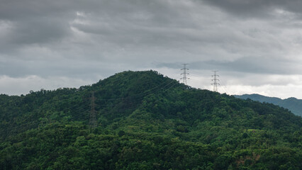 Obraz premium High-voltage power lines stretch across dense tropical greenery under a dramatic