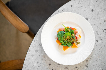 A delicious and healthy salad with pumpkin, spinach, and pumpkin seeds on a white plate, shot from a high angle on a modern stone tabletop