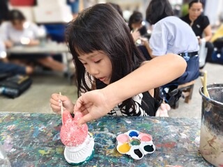 cute little thai Girl Painting a Ceramic Figurine at Table