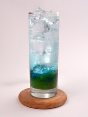 A refreshing iced soda drink with green syrup and butterfly pea flowers arranged in layers. A refreshing iced rainbow drink in a long glass.