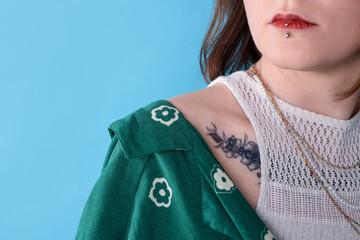 Young woman with piercings, tattoos and stylish clothes posing on light blue background, closeup....