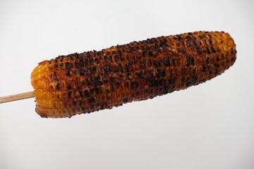 Charred and smoky grilled corn on the cob served on a stick, isolated against a white background, ideal for food and BBQ themes.	