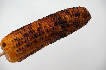 Charred and smoky grilled corn on the cob served on a stick, isolated against a white background, ideal for food and BBQ themes.	