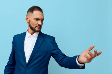 A focused business professional stands against an isolated colored backdrop, projecting confidence and calm as he gestures with an open palm toward the viewer.
