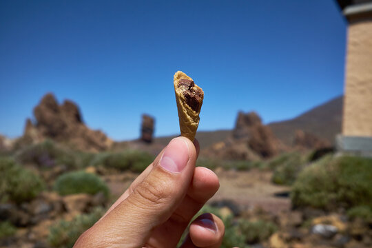 Close-up shot of human fingers holding tip of ice-cream waffle cone against picturesque background of rocky terrain