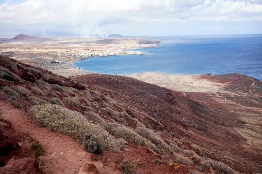 Discovering Tenerife: unforgettable view of pretty coastal town, deep blue water surface of Atlantic Ocean and cloudy sky