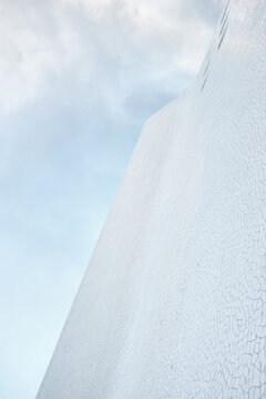 Low angle view of tall building with white mosaic outer walls and small windows stretching towards cloudy grey sky