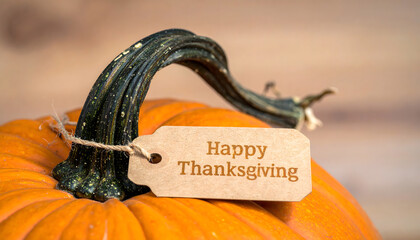 A bright orange pumpkin sits on a wooden surface with a tag that reads Happy Thanksgiving. A warm and festive image symbolizing gratitude, autumn harvest, and the spirit of Thanksgiving celebration.
