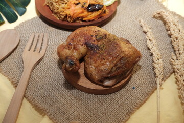 Close-up of a juicy grilled chicken leg seasoned with spices, placed on a round wooden board with a rustic background setting.

