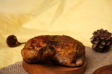 Close-up of a juicy grilled chicken leg seasoned with spices, placed on a round wooden board with a rustic background setting.

