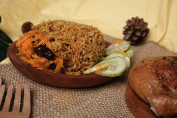 Traditional Indonesian-Middle Eastern fusion dish Nasi Kebuli, served with sliced cucumber and carrots on a rustic wooden plate over burlap.