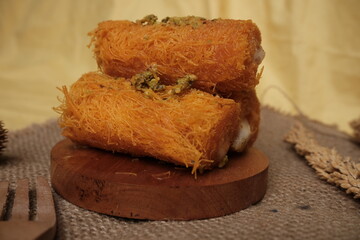 Traditional Middle Eastern kunafa rolls made with shredded phyllo dough, filled with cream, and garnished with crushed pistachios on top.
