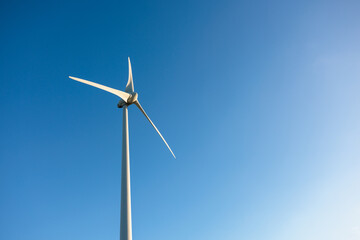 Wide landscape of multiple wind turbines aligned across fields under a cloudless blue sky. Renewable energy, infrastructure, and rural environment; no people.