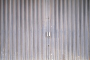 Industrial-style metal folding gate with vertical corrugated lines and central handles, commonly used for shopfronts or warehouse entrances.
