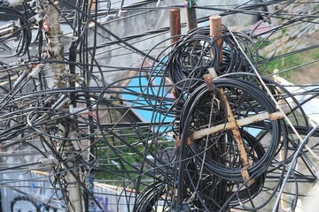 Tangled and cluttered power and communication cables on utility poles in a city setting, showing infrastructure disorder and urban complexity.
