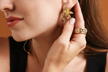 Woman wearing stylish ring and earring on brown background, closeup