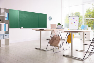 Green chalkboard and stylish furniture in classroom. Mockup for design