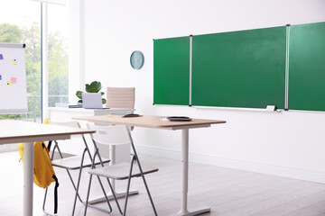 Green chalkboard, desks and chairs in classroom. Mockup for design