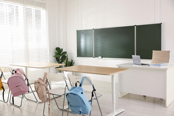 Green chalkboard, backpacks and stylish furniture in classroom. Mockup for design