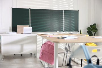 Green chalkboard, desks and chairs with backpacks in classroom
