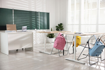 Green chalkboard, desks and chairs with backpacks in classroom
