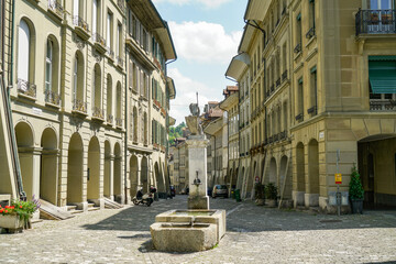 A small fountain is in the middle of a narrow street in Bern Switzerland