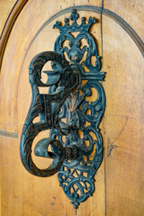 An antique metal door handle with numerous patterns on a brown wooden door in the city of Bern, Switzerland