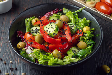 Fresh colorful vegan salad with green leaves and red bell pepper served in black plate on dark wooden table, healthy vegetarian meal for detox diet and clean eating close-up