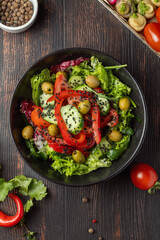 Fresh colorful vegan salad with green leaves and red bell pepper served in black plate on dark wooden table, healthy vegetarian meal for detox diet and clean eating close-up