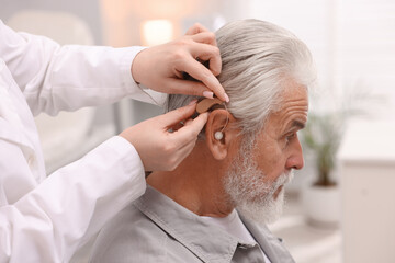 Obraz premium Doctor putting hearing aid into senior man's ear in hospital, closeup