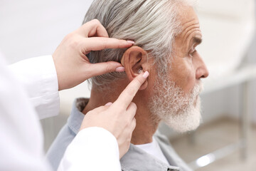 Fototapeta premium Doctor putting hearing aid into senior man's ear in hospital, closeup