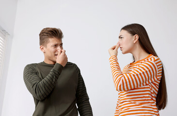 Unhappy couple suffering from bad smell and covering their noses indoors