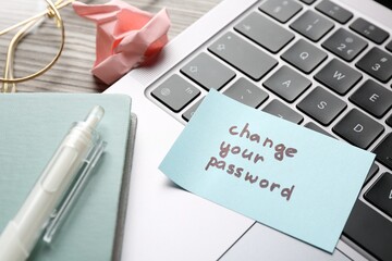 Note with phrase Change your password, notebook, pen, glasses and laptop on wooden desk, closeup