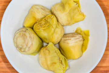 Canned green artichoke in bowl on cutting board, top view