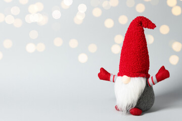 Funny Christmas gnome on light grey background with blurred lights, closeup. Space for text