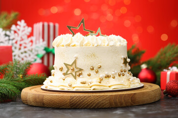 Delicious cake with Christmas decor on black table against red background with blurred lights, closeup