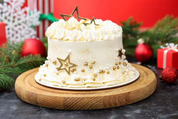 Delicious cake with Christmas decor on black table against red background, closeup