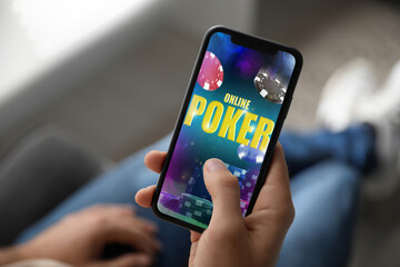 Man playing online poker on mobile phone indoors, closeup