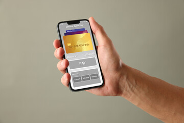 Online payment. Man holding mobile phone with open app in hand on grey background, closeup