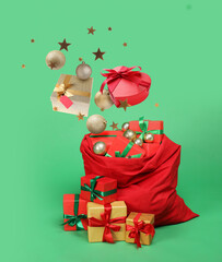 Christmas balls and gift boxes falling into red Santa bag on green background