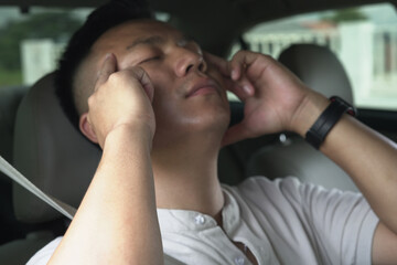 An asian male driver getting exhausted and feeling headache, wrist pain, neck ache, shoulder pain and backache, sitting inside his car, after driving car in traffic jam, causing stressed and anxiety.	