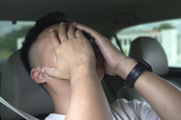 An asian male driver getting exhausted and feeling headache, wrist pain, neck ache, shoulder pain and backache, sitting inside his car, after driving car in traffic jam, causing stressed and anxiety.	