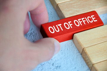 Hand pulling out a red wooden block with out of office text on. Getaway or on a vacation concept.