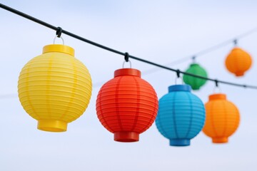 Obraz premium Colorful Paper Lanterns Hanging Outdoors Against a Soft Blue Sky, Perfect for Festive Celebrations