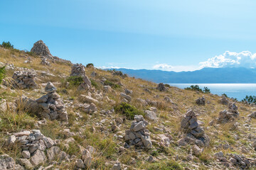 Scenic landscape with stone cairns on sunny hillside near ocean. Hike from Baška to Vela Luka