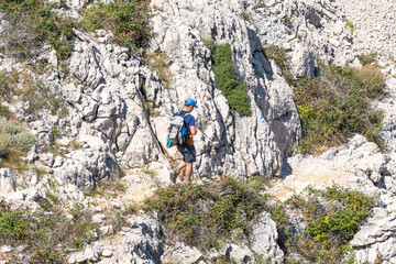 Young caucasian male hiker exploring rocky terrain in blue cap and backpack