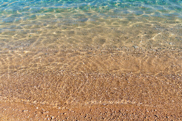 Sunlit sandy shoreline with gentle wave ripples on clear water