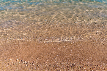 Sunlit rippling water on sandy beach with gentle waves