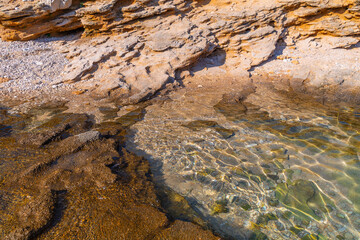 Sunlit rocky shoreline with clear water and jagged rock formations