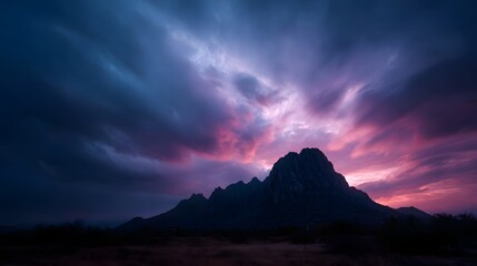 A majestic mountain peak silhouetted against a dramatic sky illuminated by vibrant pink and purple twilight clouds